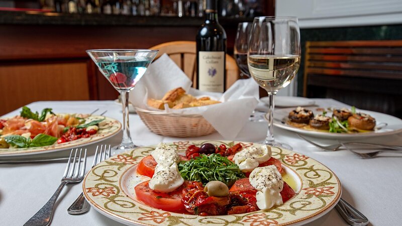 Multiple appetizers with focus on tomato and fresh mozzarella with glass of wine